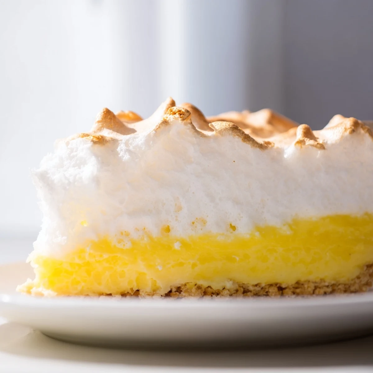 Lemon Meringue Pie with graham cracker crust is plated beside hot Earl Grey tea on a cozy table.