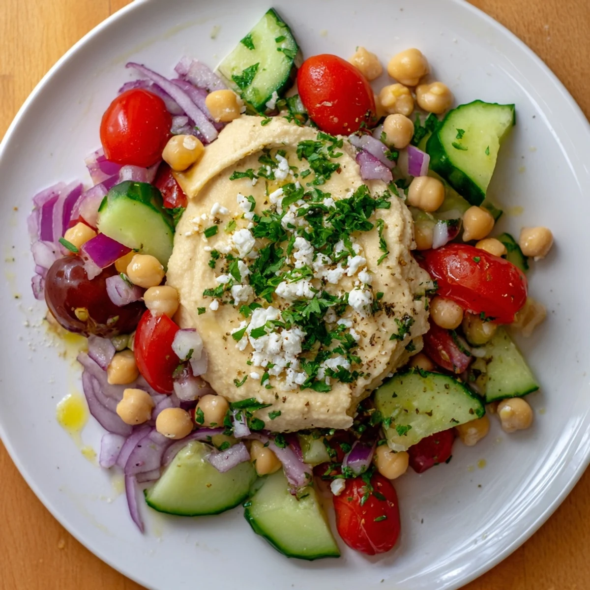 Colorful Mediterranean Salad with Hummus topped with creamy hummus dollop, parsley, and feta on a white plate.