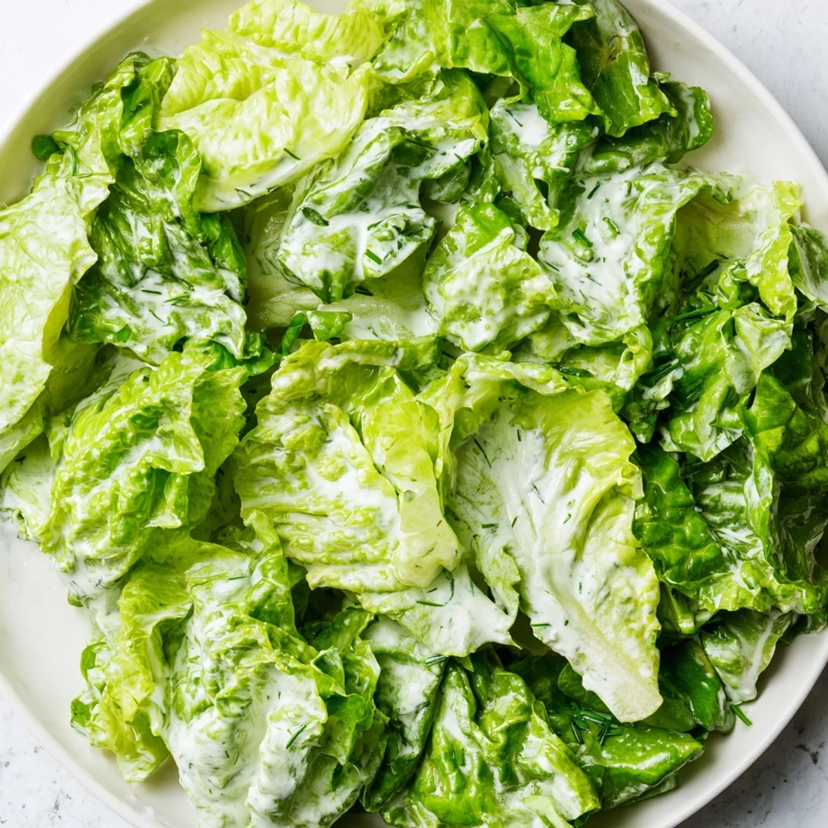 A vibrant Green Salad with Green Goddess Dressing on a white plate, featuring crisp greens, sliced radishes, and creamy avocado slices.