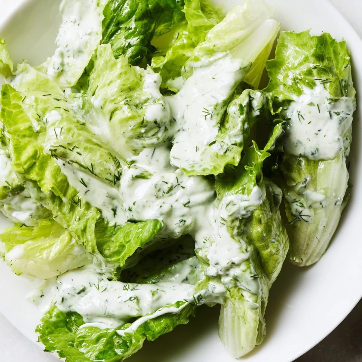 A close-up of Green Salad with Green Goddess Dressing drizzled over romaine, baby spinach, and cucumber, showcasing a creamy, bright green hue.