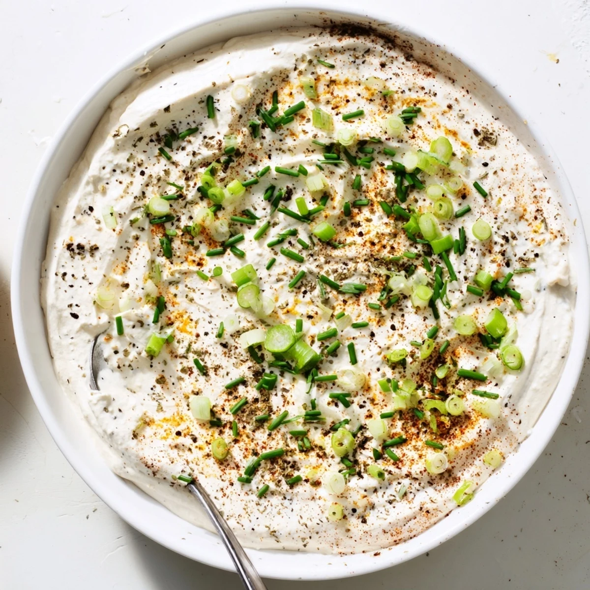 A bowl of creamy snack cheese dip garnished with fresh chives, served with crunchy crackers and colorful veggie sticks.