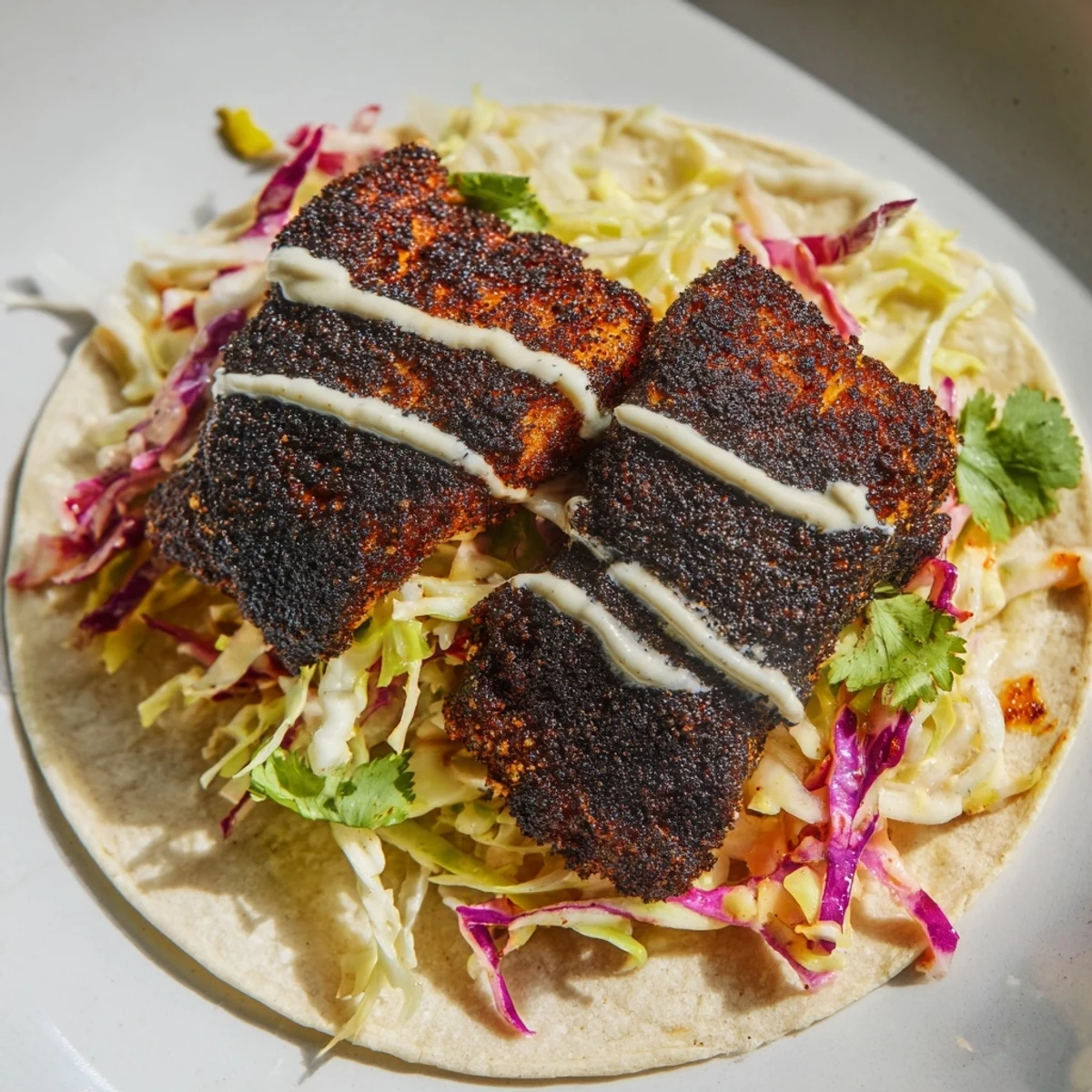 Golden-brown Louisiana blackened fish tacos with creamy slaw and drizzled sauce on a plate.