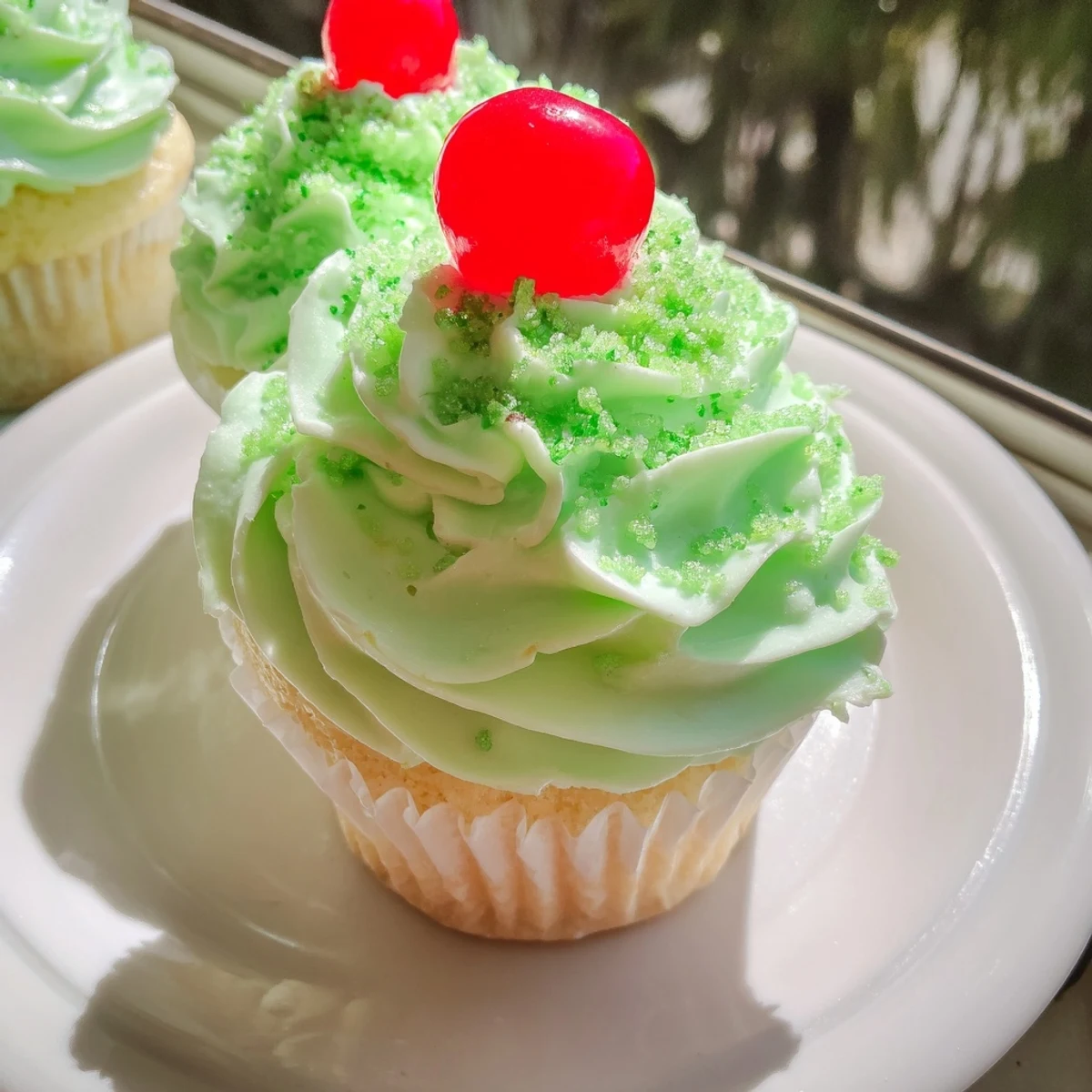 Glazed Shamrock Shake Cupcakes sit on a white plate, showcasing their fluffy texture and vibrant, creamy mint frosting.