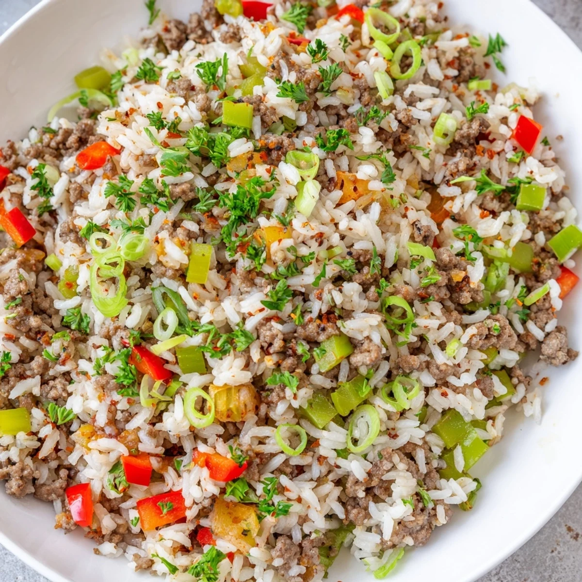 A close-up of Cajun Dirty Rice with Ground Beef and Peppers reveals fluffy grains, peppers, and spices in a rustic cast-iron skillet.