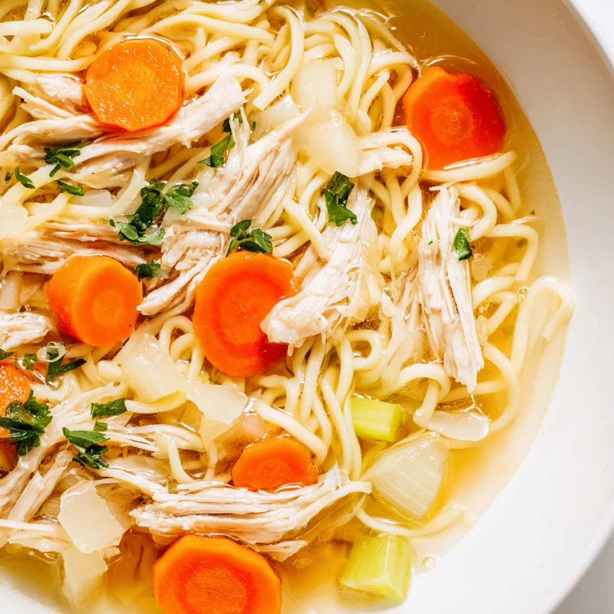 Steam rises from Chicken Noodle Soup with Homemade Noodles, revealing colorful carrots and celery in a rustic kitchen setting.