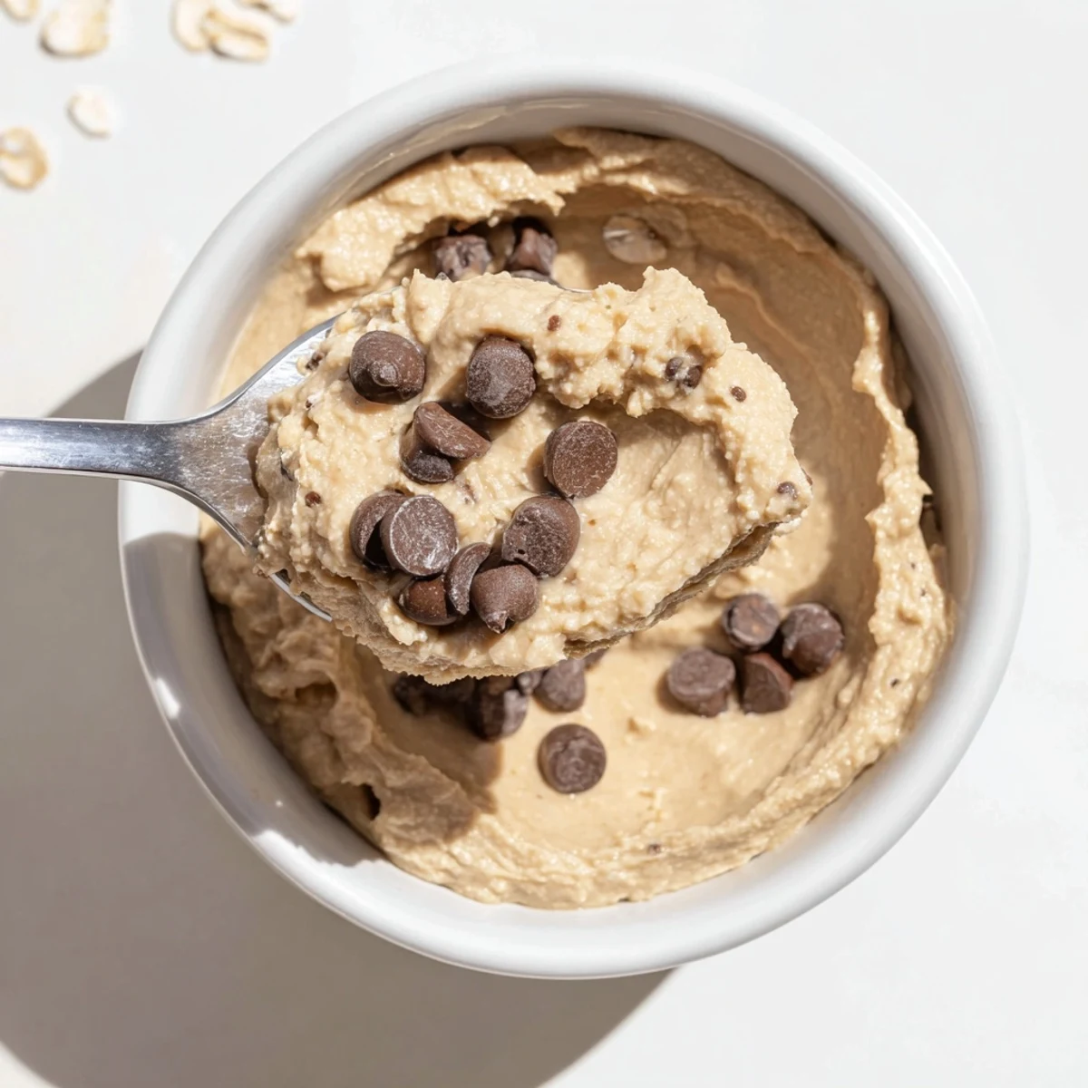 A wooden spoon scoops into homemade Chocolate Chip Cookie Dough Hummus with oats and chocolate chips.