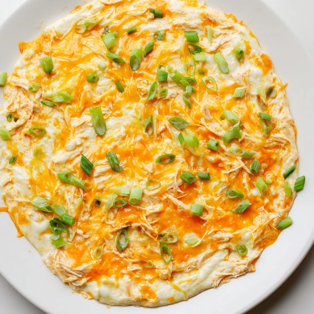 A warm bowl of Spicy Buffalo Chicken Dip topped with sliced green onions, surrounded by crispy tortilla chips for dipping.