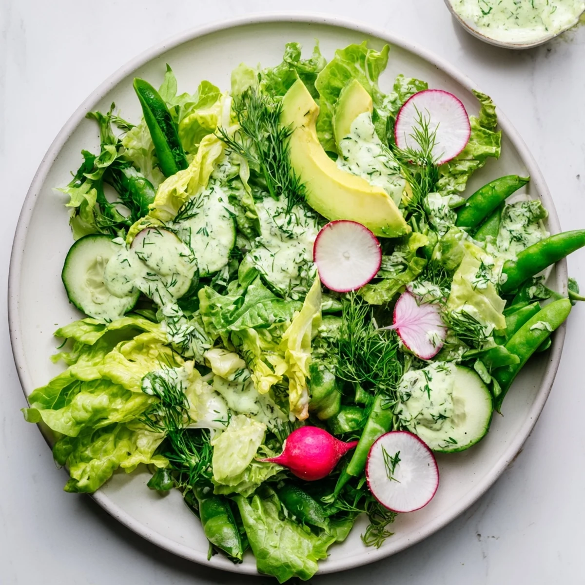 A vibrant Green Salad with Green Goddess Dressing featuring crisp romaine and creamy avocado slices on a wooden table.