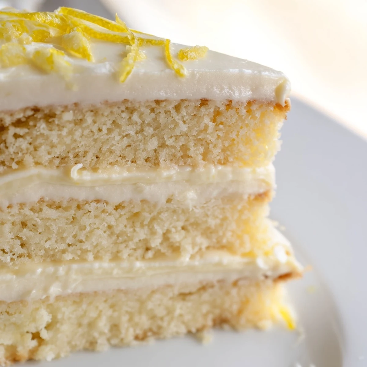 A close-up view of a slice of Limoncello Mascarpone Cake, revealing delicate crumb and mascarpone filling garnished with fresh lemon zest.
