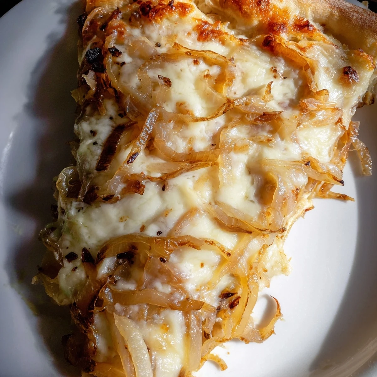 A close-up of caramelized onion pizza with melty cheese bubbling on a golden crust, served on a rustic wooden board.