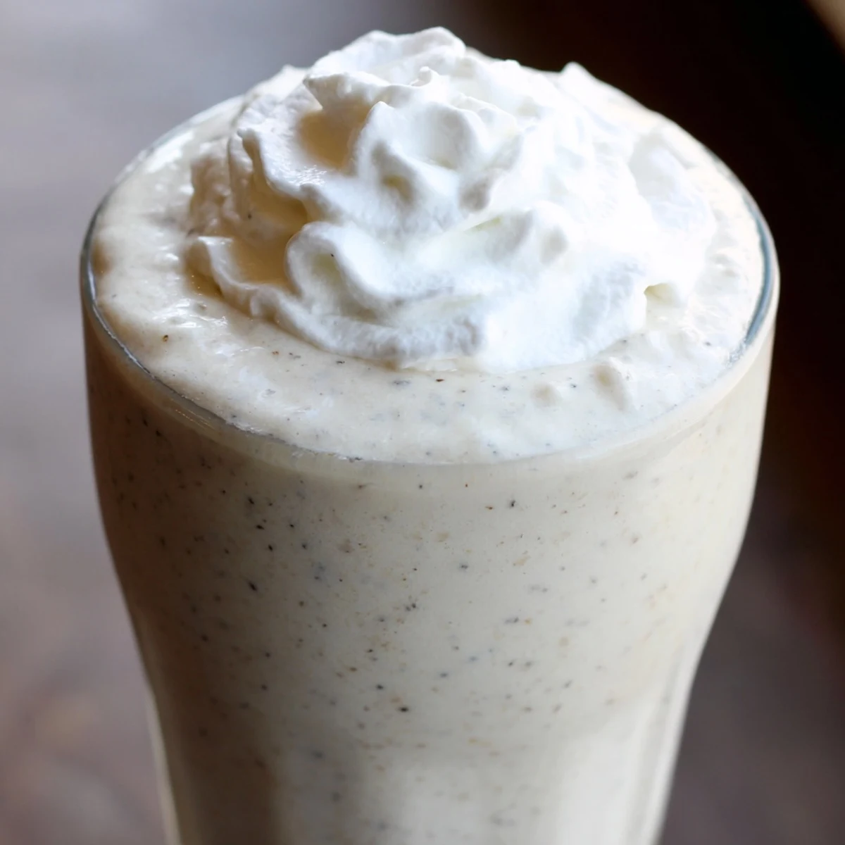 This Starbucks Vanilla Bean Frappuccino is served in a tall glass with a straw beside a bowl of ice cubes.
