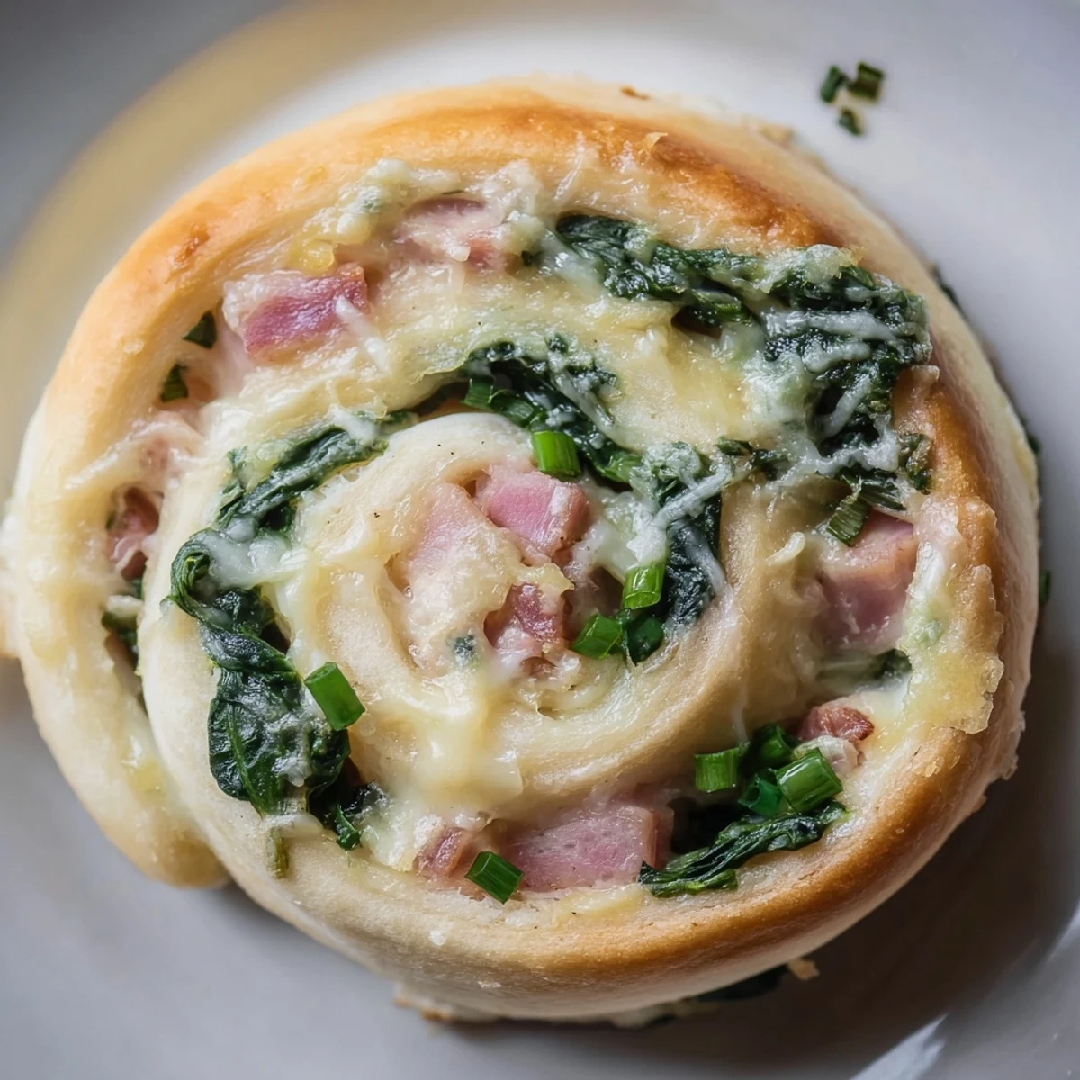 Golden-brown Savory Spinach and Ham Breakfast Rolls sit in a baking dish, showcasing flaky crust and melted cheese with fresh spinach peeking through the layers.