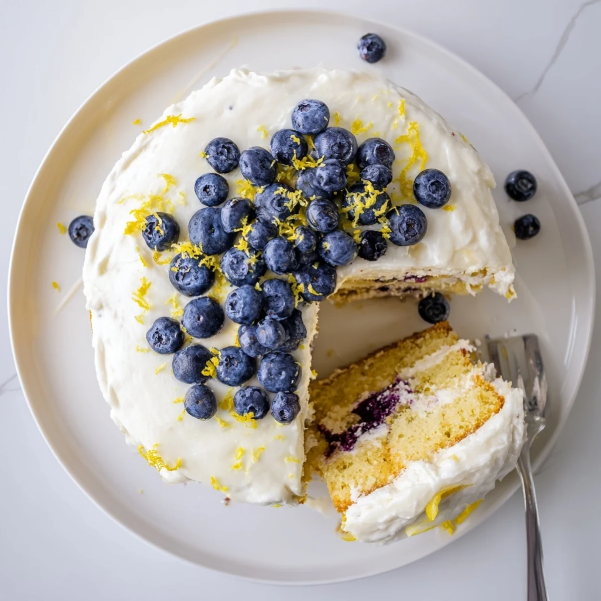 Elegant Lemon Blueberry Cake with Cream Cheese Frosting is topped with berries and zest, ready for spring or summer gatherings.