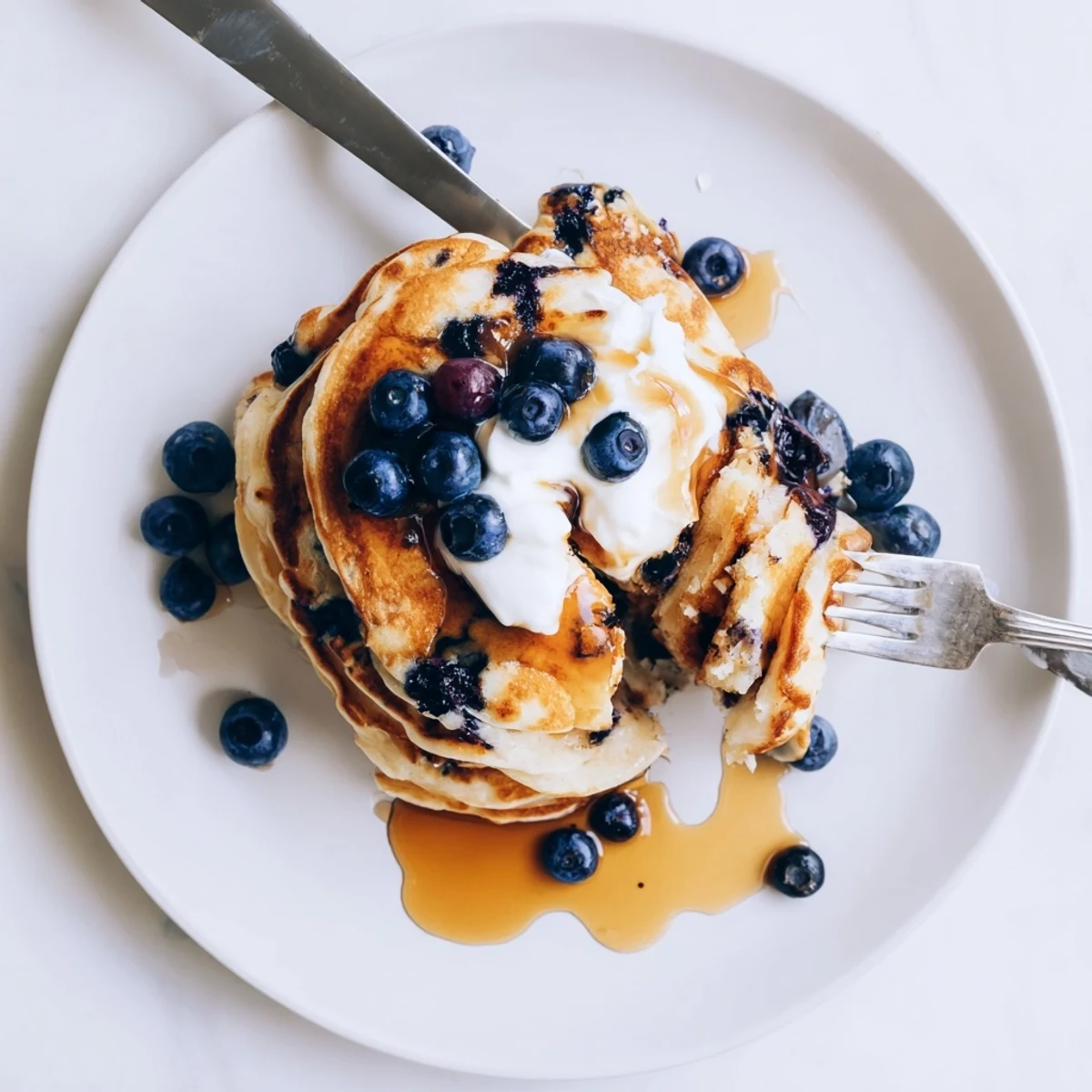 Stack of fluffy Greek yogurt blueberry pancakes topped with fresh berries and maple syrup