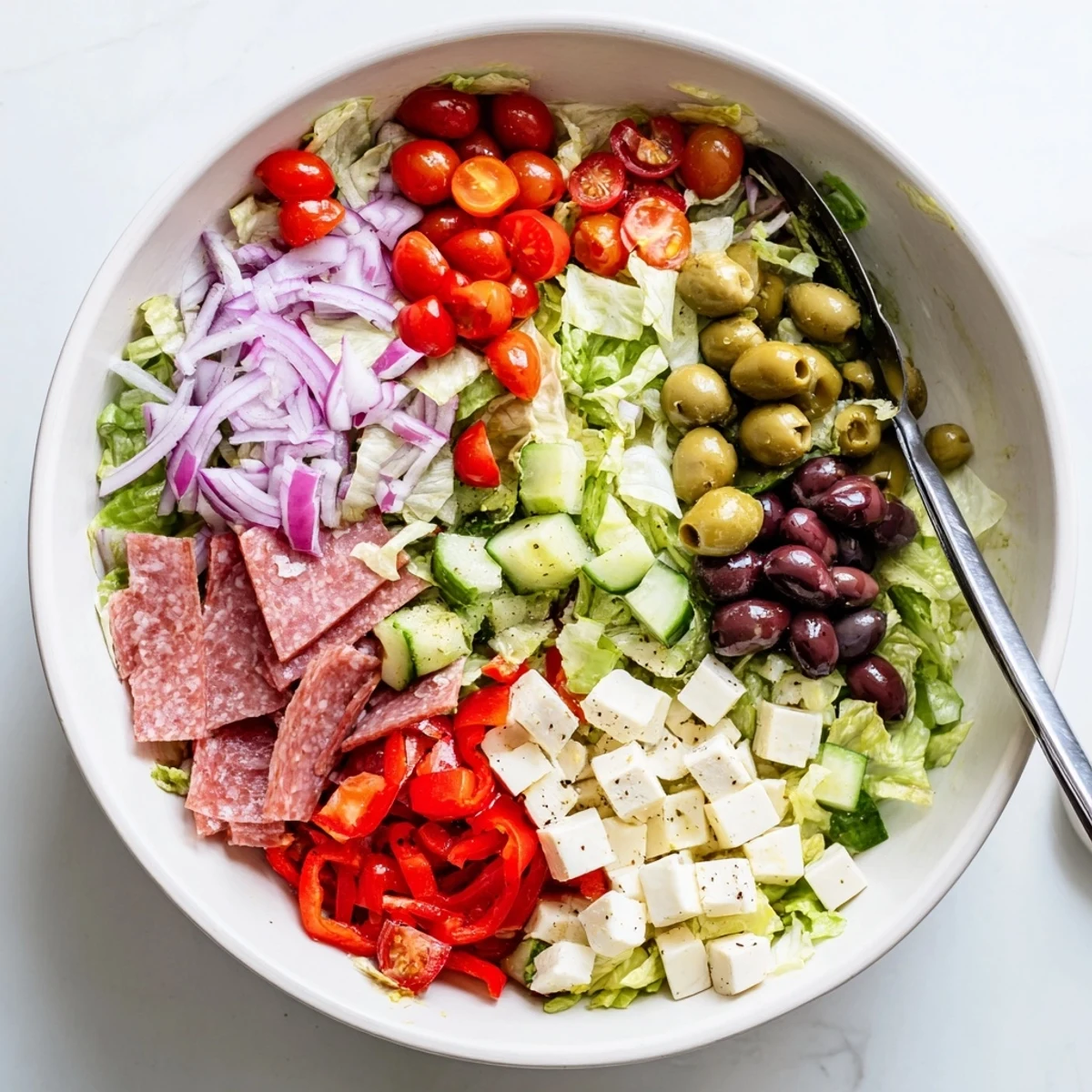 Colorful Italian chopped salad bowl with crisp romaine, tomatoes, salami, olives, and mozzarella in zesty homemade dressing