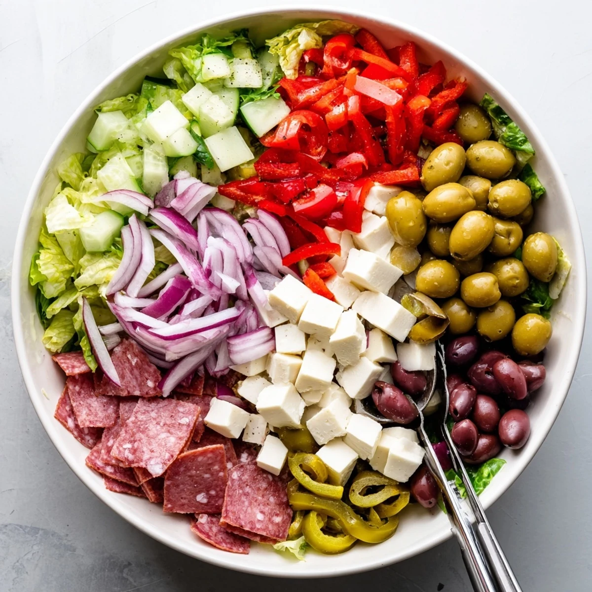 Heaping bowl of Italian chopped salad tossed with Genoa salami cubes, Kalamata olives, cucumber, and vibrant homemade dressing
