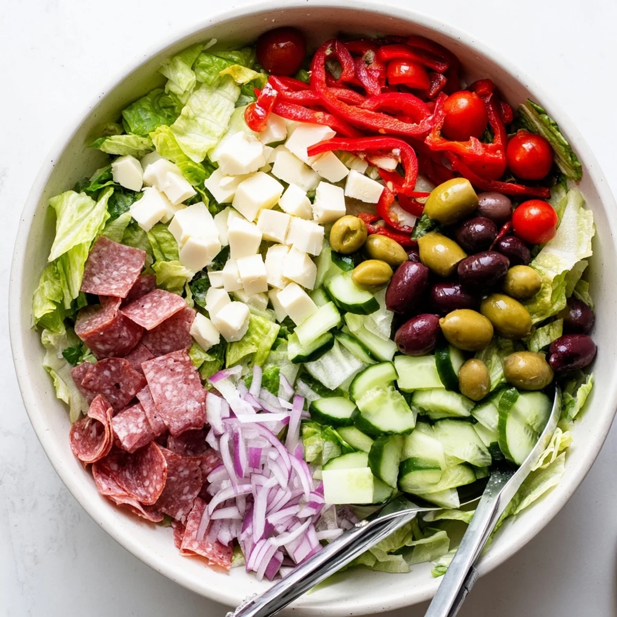 Fresh Italian chopped salad arranged on white plate featuring pepperoncini, red peppers, parmesan, and tangy vinaigrette