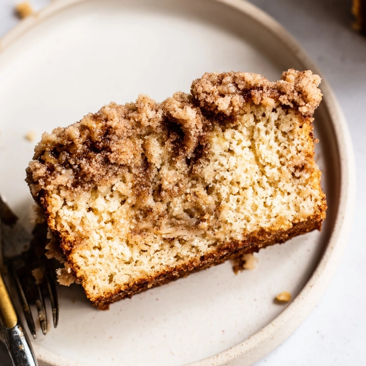 Warm slice of cinnamon crumb banana bread on a white plate with melting butter