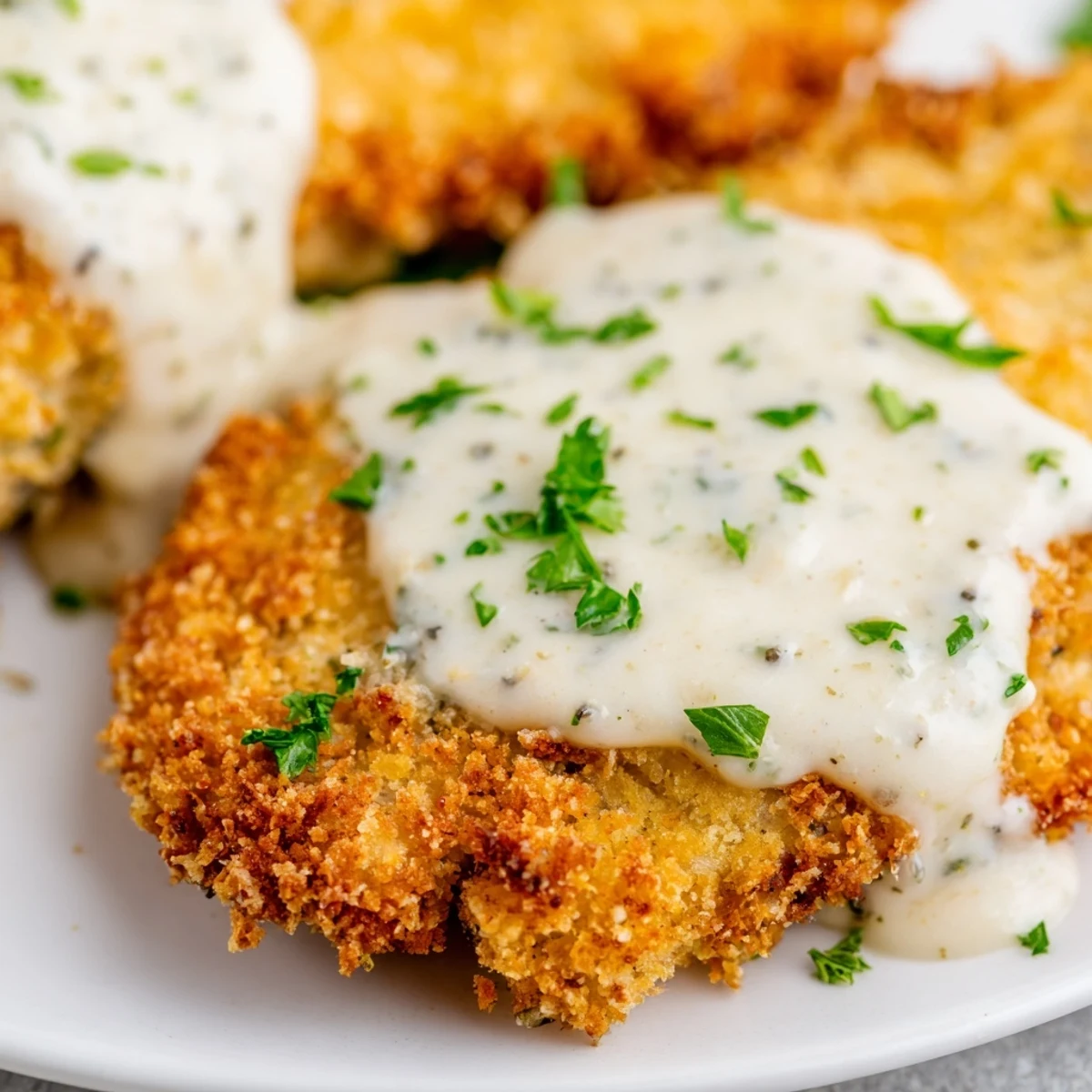 Golden Parmesan crusted chicken breast topped with rich creamy garlic sauce on a white plate