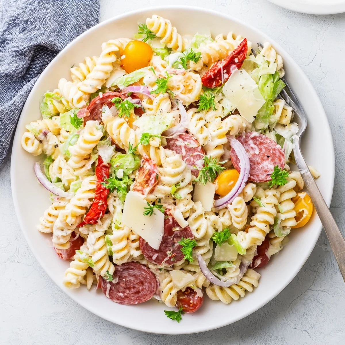Crowd-pleasing Italian Grinder Pasta Salad bowl packed with deli meats, roasted red peppers, red onion, and Parmesan garnish