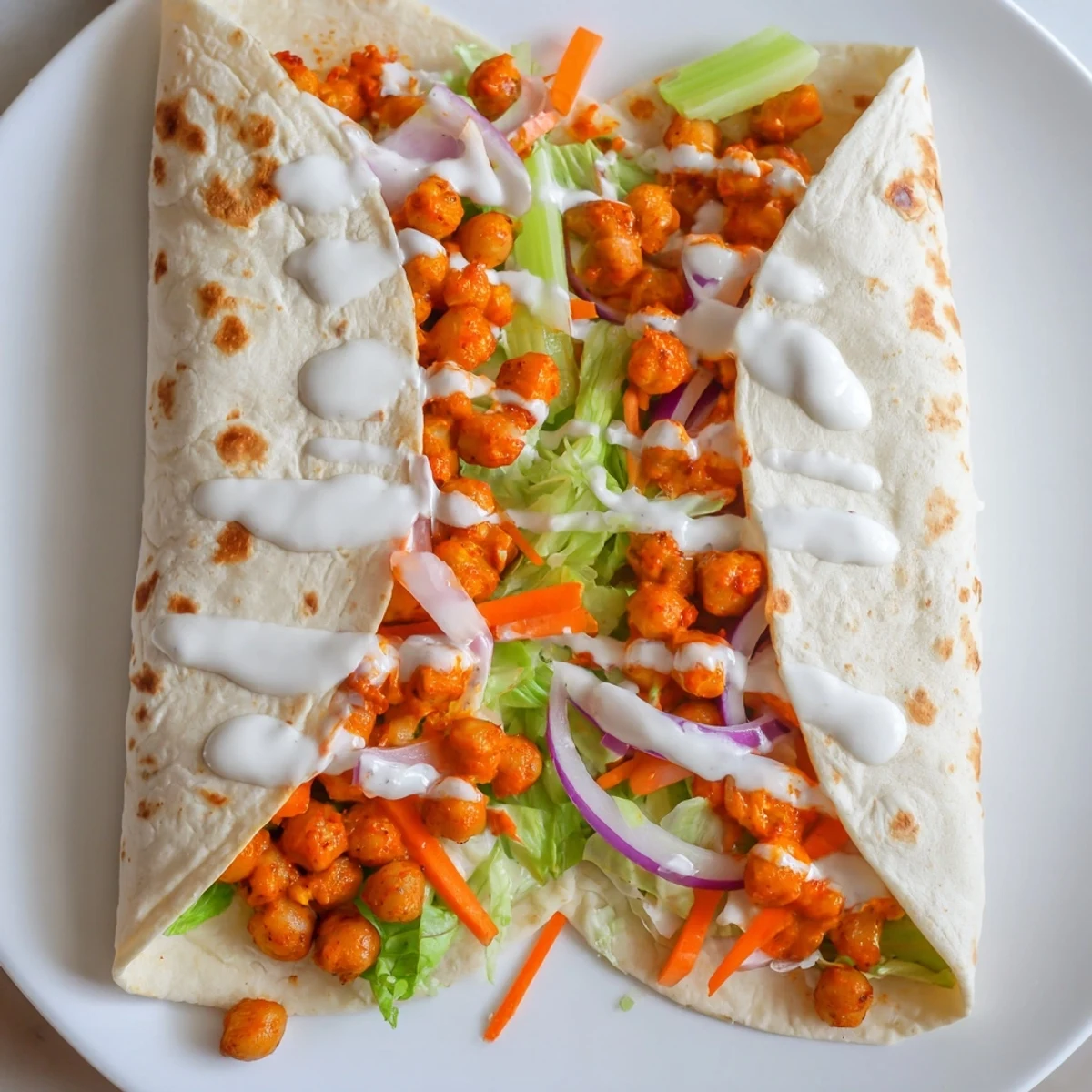 Vegetarian buffalo chickpea wraps layered with colorful vegetables and drizzled with creamy dressing