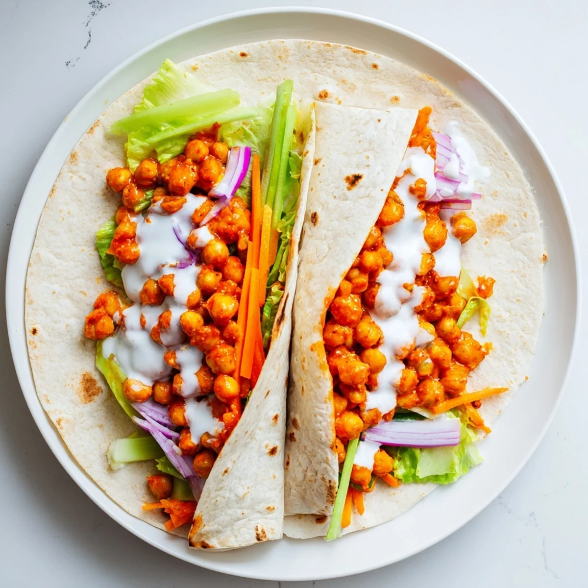 Spicy buffalo chickpea wraps rolled with fresh lettuce, crunchy carrots, and tangy sauce