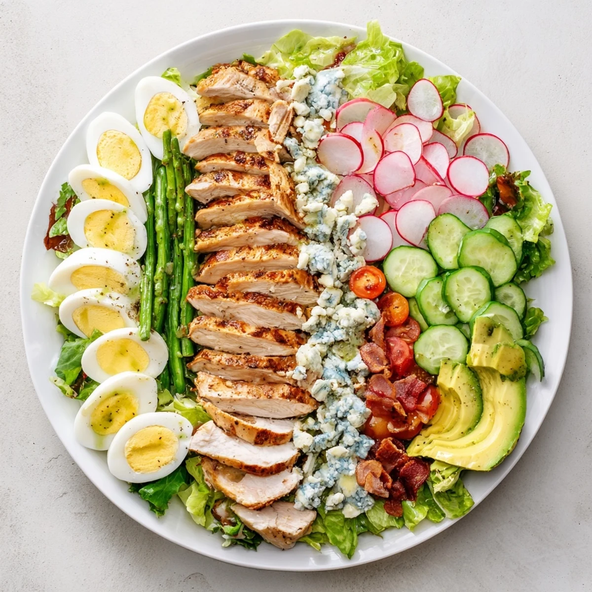 Vibrant Spring Cobb Salad plated with rows of avocado, cherry tomatoes, cucumber, and herb vinaigrette drizzled over mixed greens