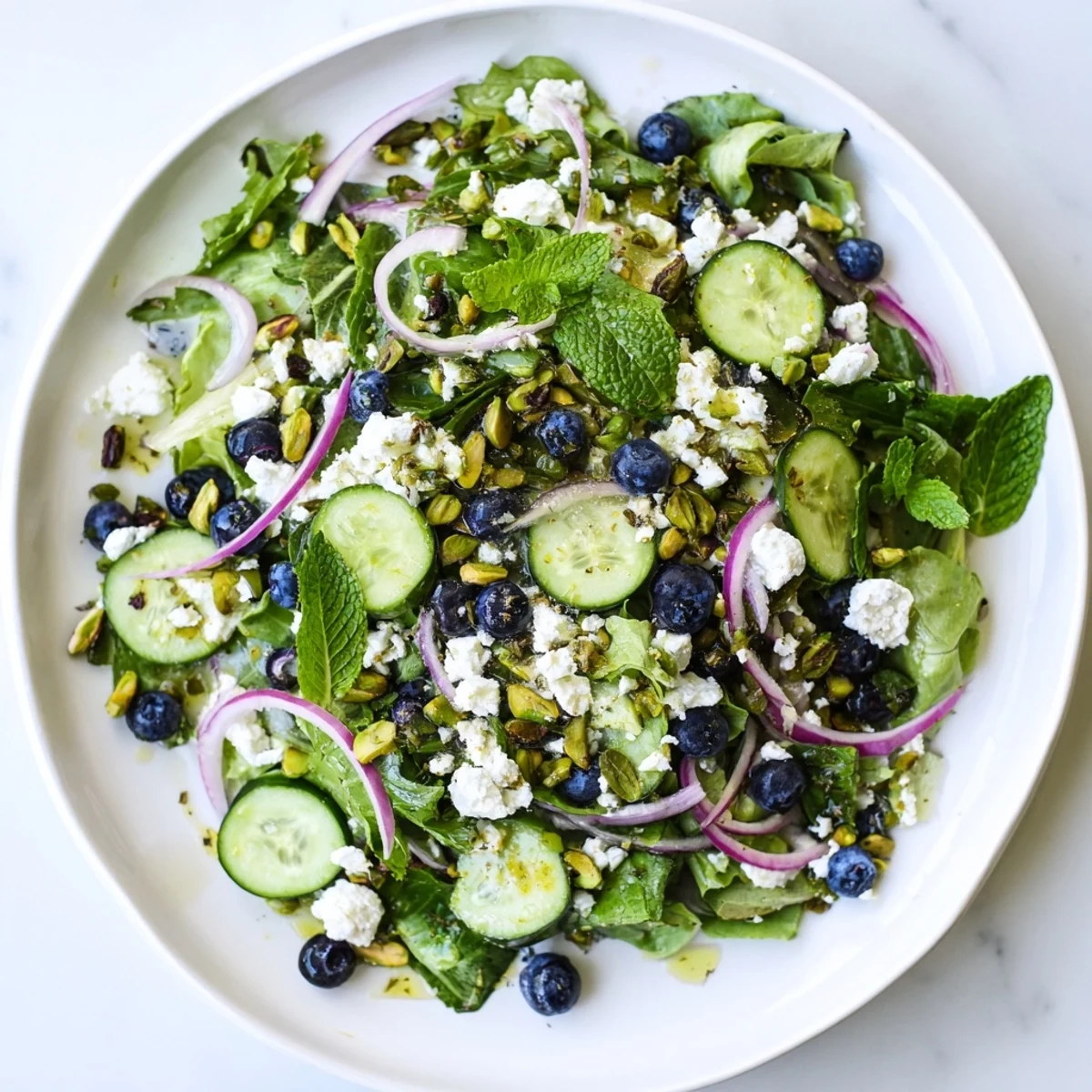 Colorful blueberry pistachio spring salad with fresh greens, feta, cucumber, and light lemon-honey dressing