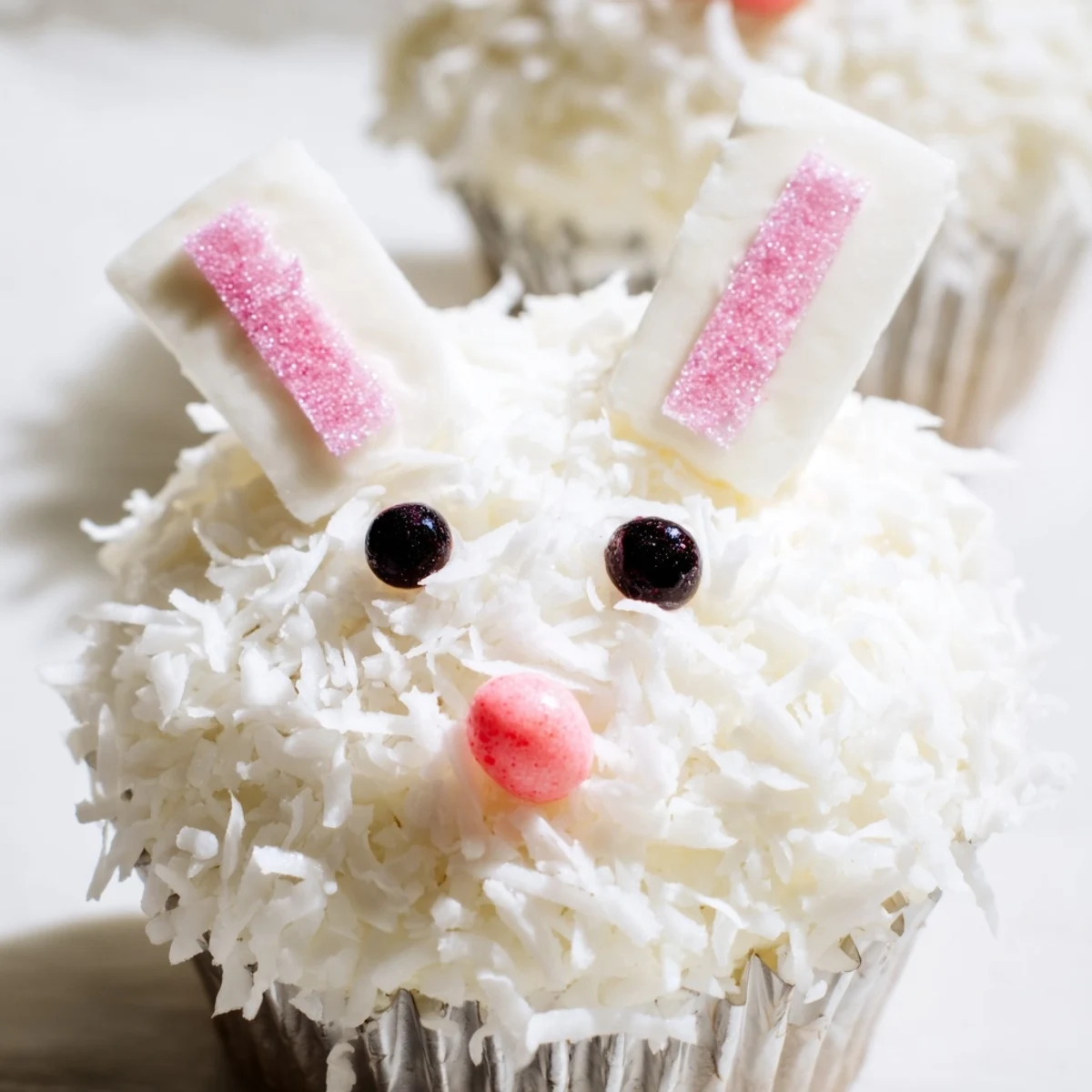 Frosted bunny cupcakes decorated with candy eyes, pink jelly bean noses, and shredded coconut