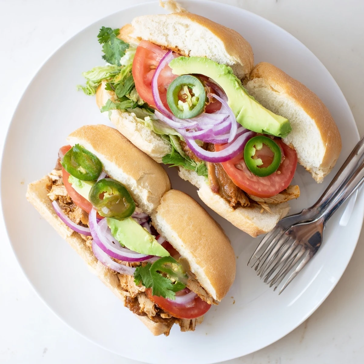 Golden sliced chicken torta sandwich stacked with avocado and fresh vegetables on a bolillo roll