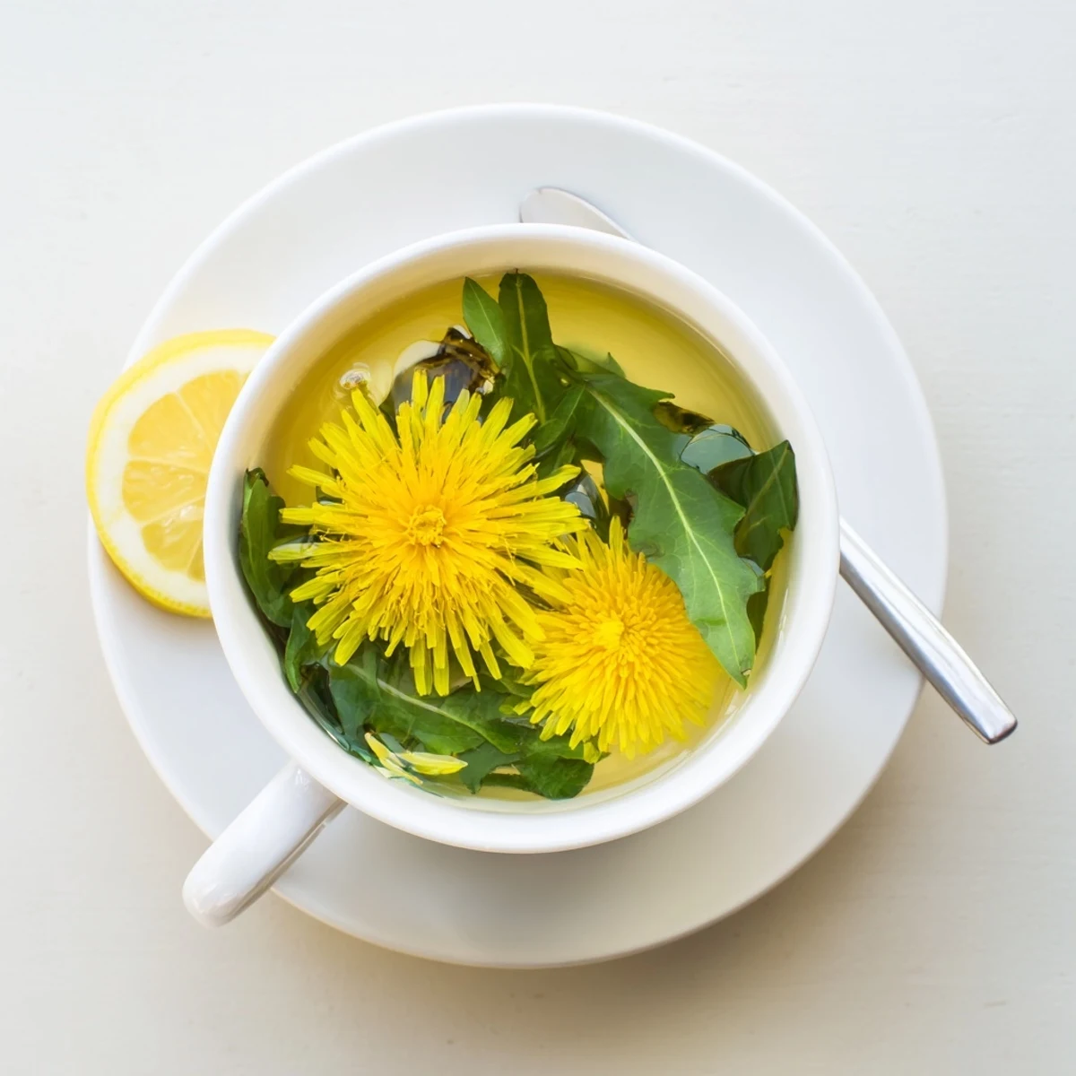 Golden dandelion tea steaming in a white ceramic cup with fresh green petals scattered nearby