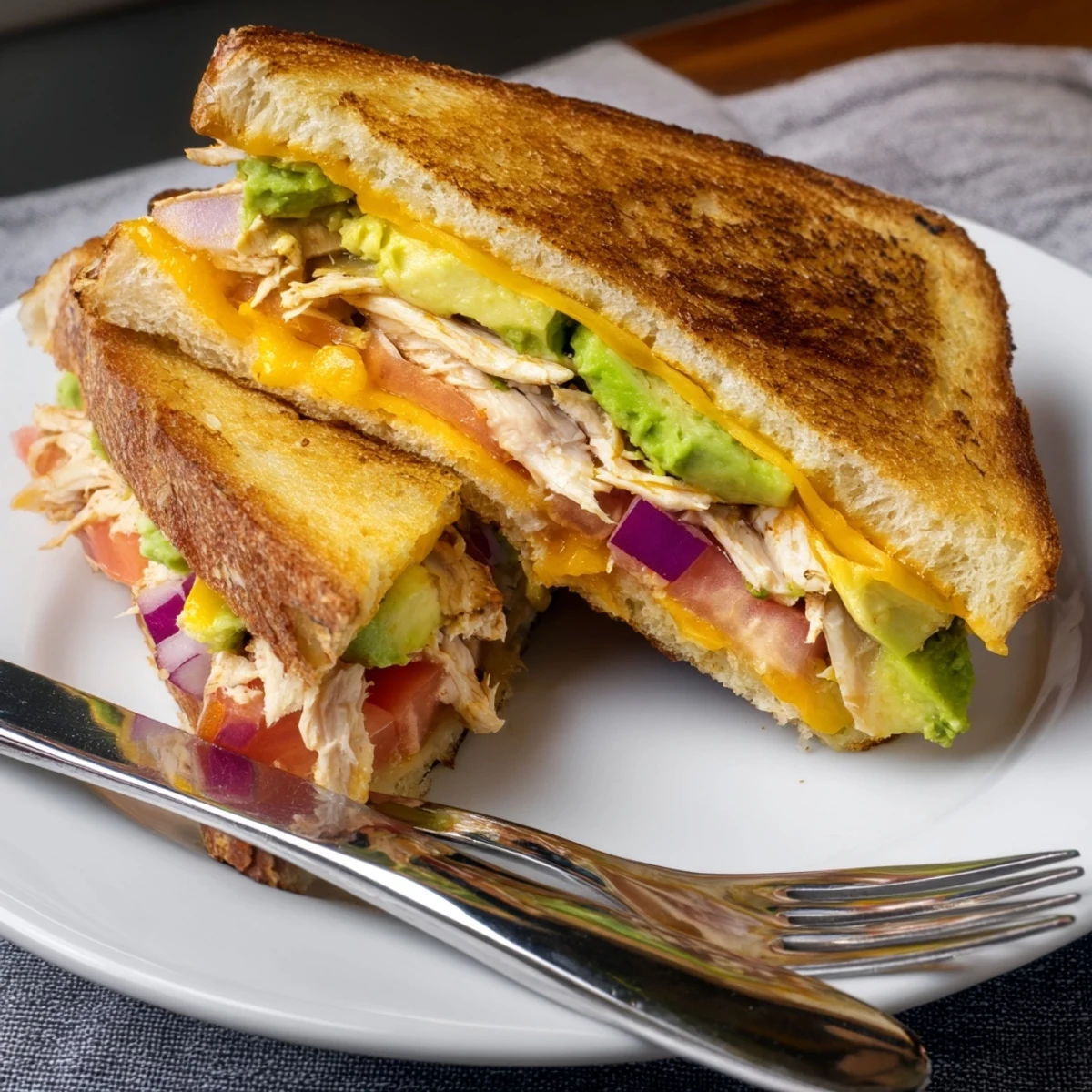 Warm chicken avocado melt sandwich served on a plate with fresh tomato and red onion