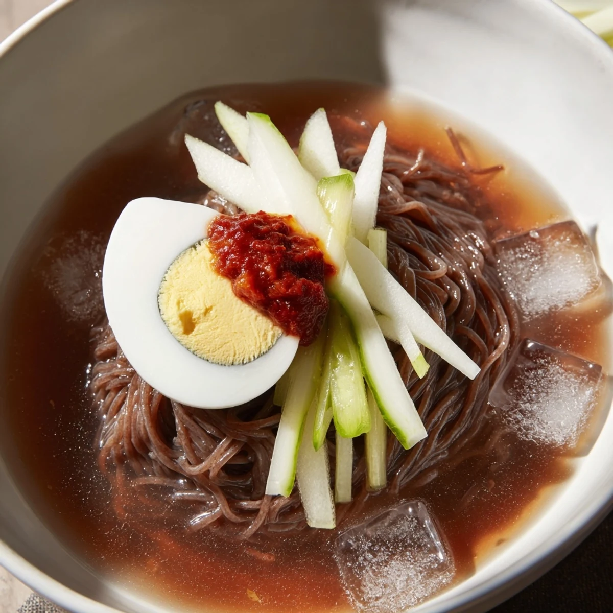 Buckwheat Korean naengmyeon cold noodle soup garnished with egg, beef, and Asian pear