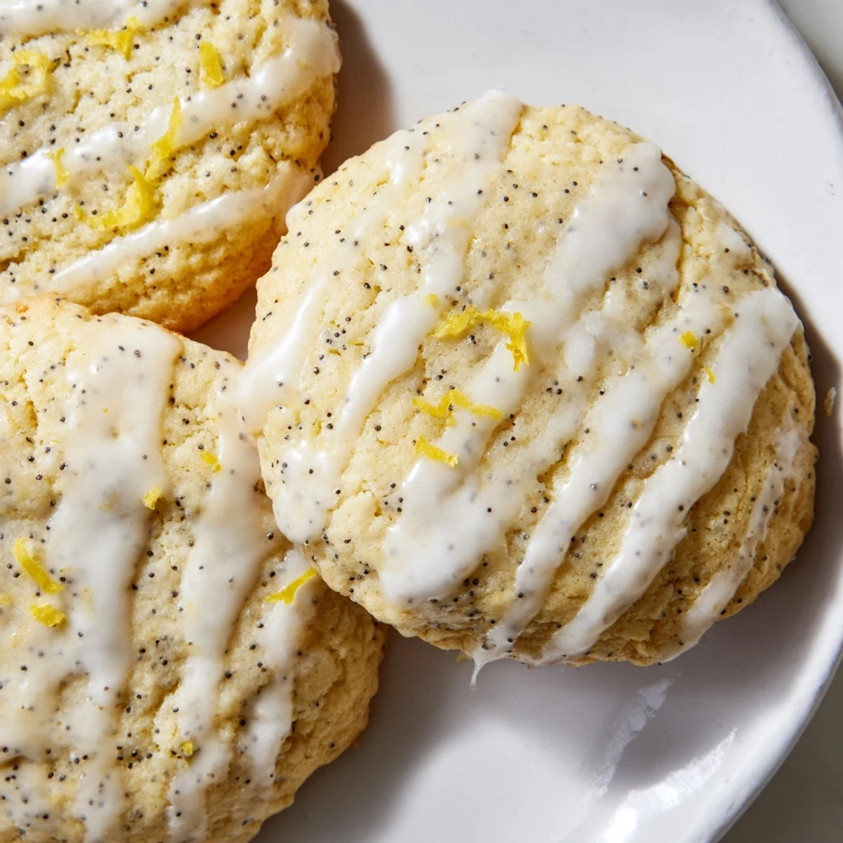 Golden lemon poppy seed cookies with crackly tops drizzled with sweet citrus glaze on a white plate