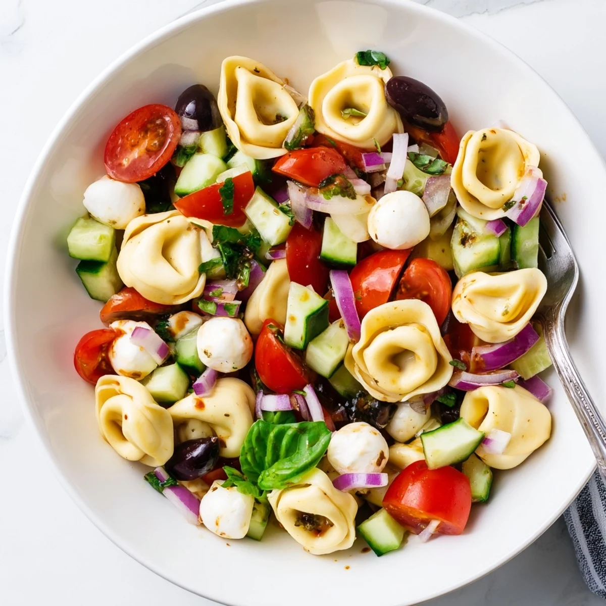 Chilled tortellini pasta salad in a white bowl garnished with mozzarella balls