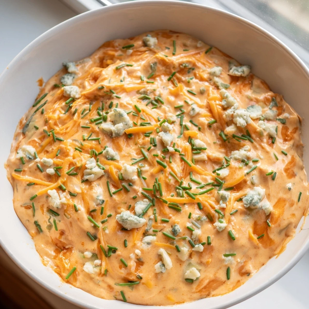 Creamy buffalo pickle dip in a serving bowl surrounded by crunchy chips and fresh veggie sticks for dipping