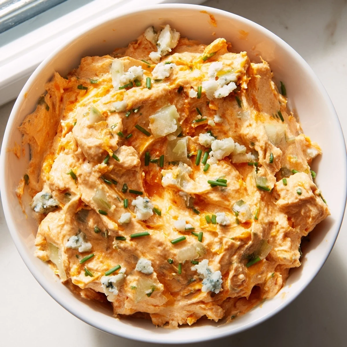 Tangy buffalo pickle dip topped with diced pickles and chives served in a rustic ceramic bowl