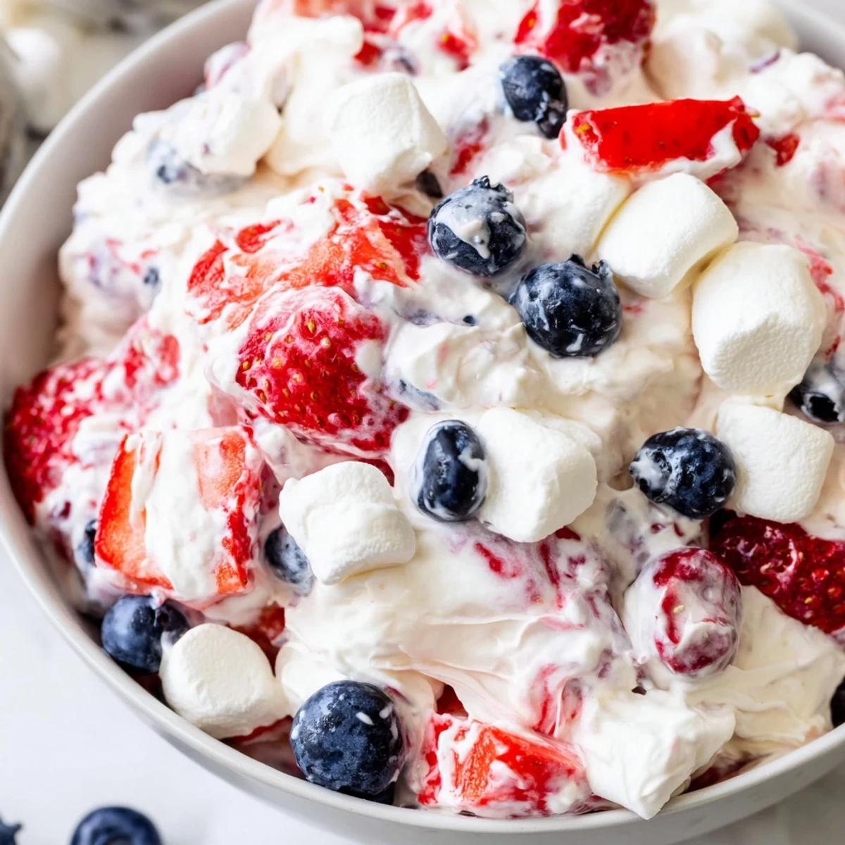 Vibrant Red White Blue Cheesecake Salad scooped into a dessert glass with juicy strawberry and blueberry garnish