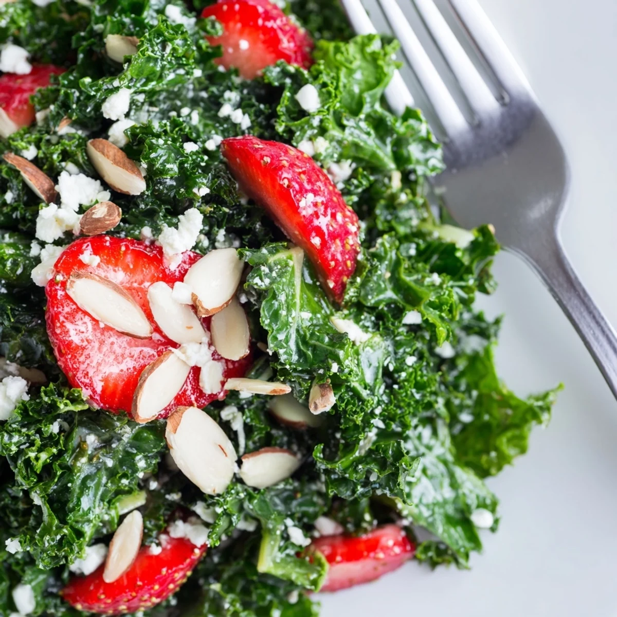 Summer kale salad topped with juicy berries, feta, and toasted almonds in a shallow bowl