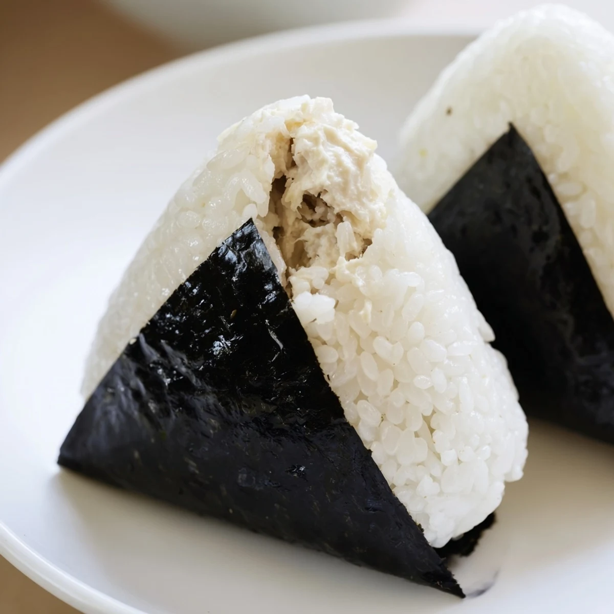 Handheld triangle shaped tuna mayo onigiri wrapped in crisp nori seaweed strips