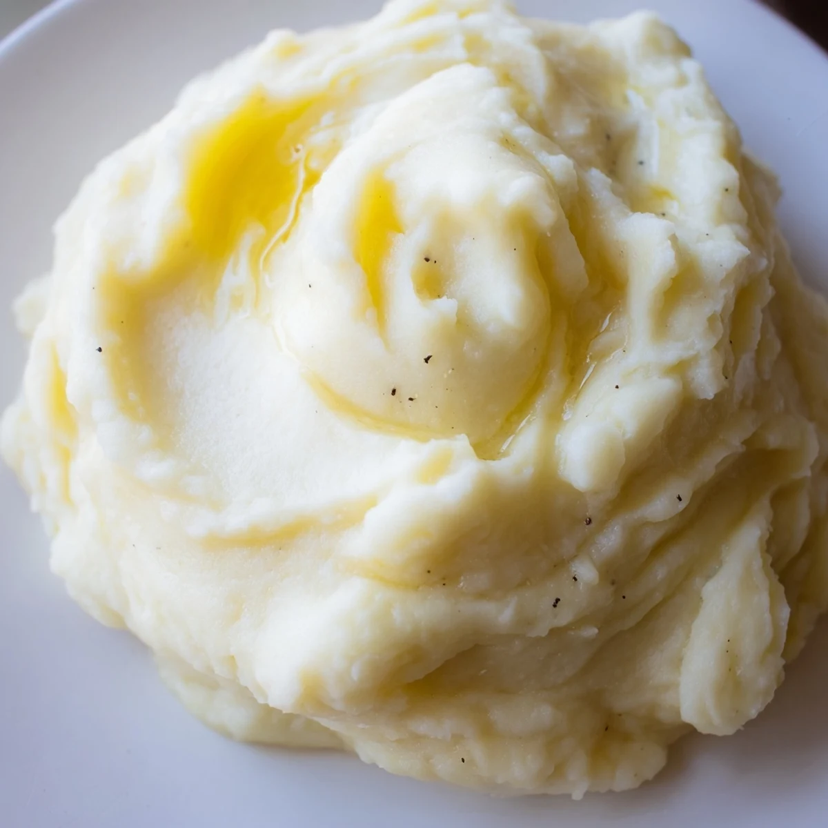 Steaming velvety mashed potatoes scooped into a serving dish beside roasted meat