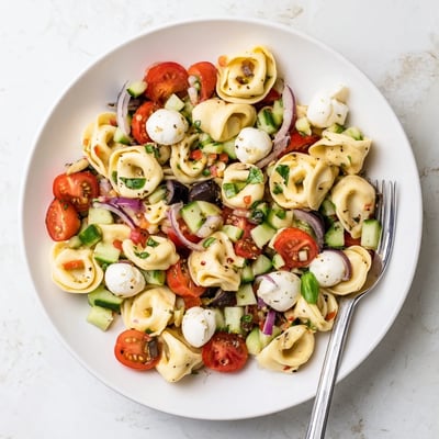 Tortellini pasta salad loaded with cherry tomatoes cucumber olives and fresh basil