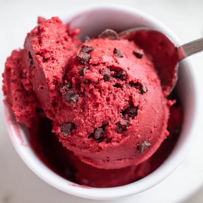 Bright red edible red velvet cookie dough topped with chocolate chips in a rustic bowl